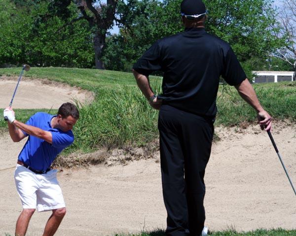 Sophomore economy major Jeremy Harris practices his shots in the sand bunker while coach Marcus Patters watches and gives pointers on April 9 at Hagen Oaks Golf Academy.: