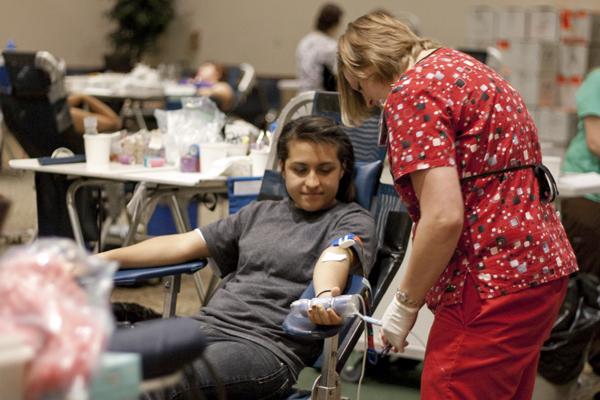 blooddrive10:A student grips tight while she gives blood as the phlebotomist checks the needle.:Tina Horton - State Hornet 