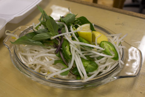 A plate of garnishes to add to the pho includes: lemon, jalapenos, bean sprouts, and mint leaves.