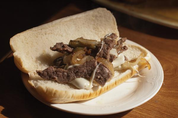 The finished Philly cheese steak sandwich is plated and ready to eat.
