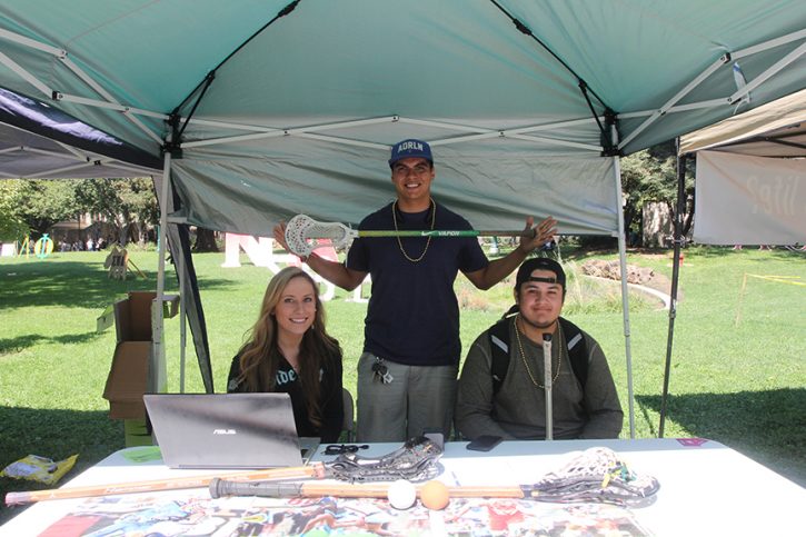 From left, Nutritional Advisor Randi McCreary, Lacrosse Club President Charles Serna and goalie Nicolas Plata-Escobar sit at the booth for their new club that brought lacrosse back. (Photo by Francisco Medina)