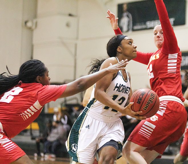 Sacramento State senior guard Ashlyn Crenshaw drives past two Stanislaus State players for a layup at the Nest on Nov. 29. (Photo by Matthew Dyer)