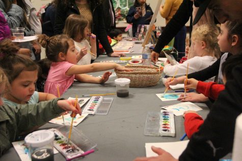 Children line a table, alternately paint with watercolors and blow through a straw on the watercolors as part of an interactive activity in the Orchard Suite during the More Than Just Scribbles art reception on Feb. 23. (Photo by Rin Carbin)