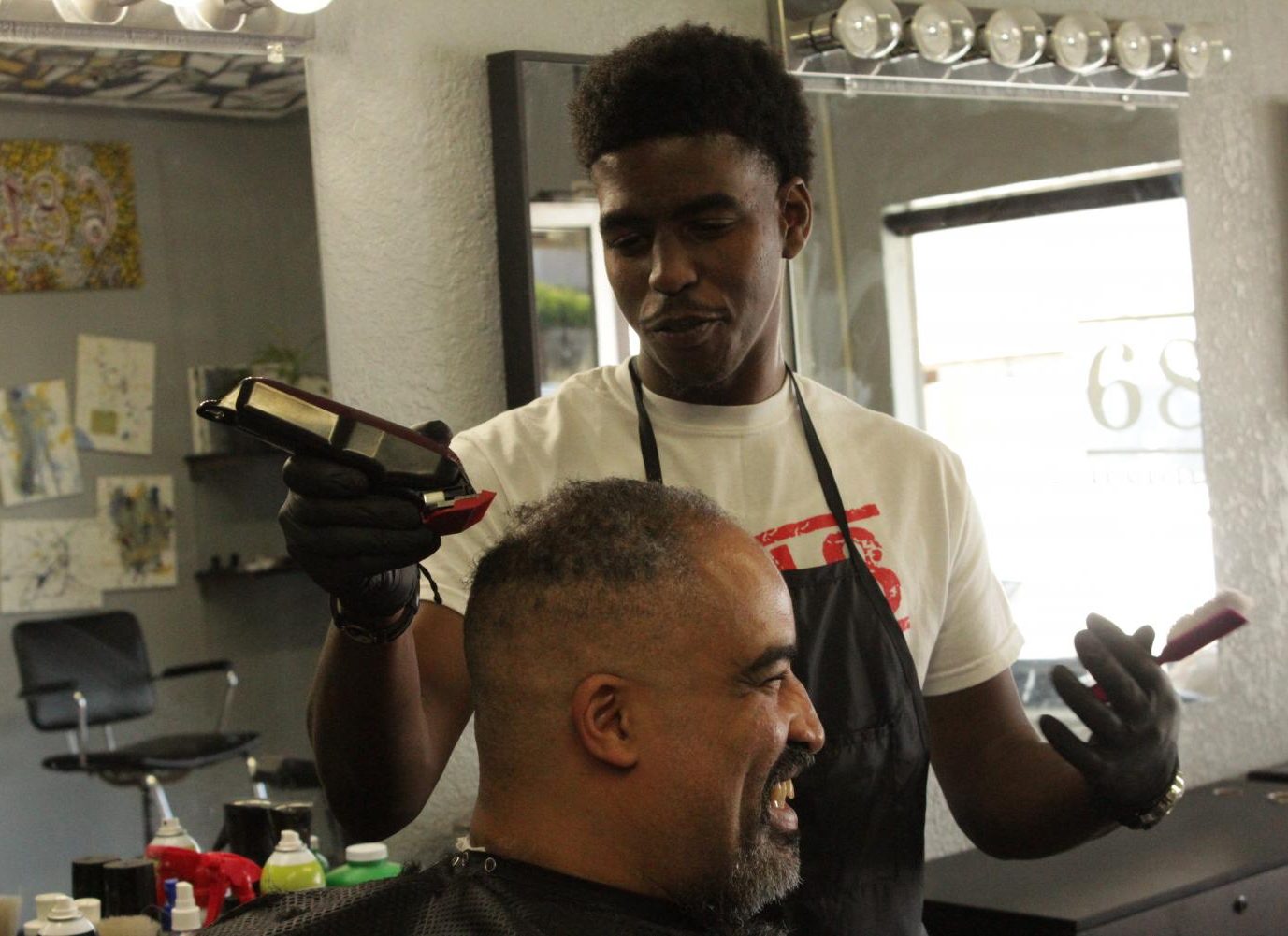 Geoffrey Ndirangu jokes with his client, Jesse Lowe, while giving him a haircut on May 1, 2018.