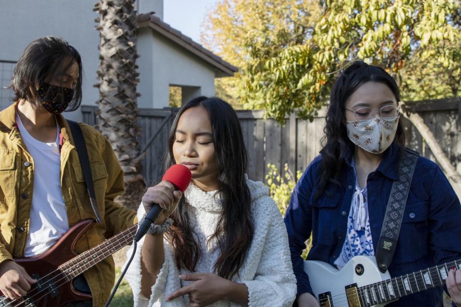The band Break Up Hoodies performs songs in a backyard in Sacramento, California, Sunday, Nov. 8, 2020. The band includes Sacramento State computer science major Lauren Mateo, center, on vocals, Devyn Farrales, left, on bass and Jasmine Rubio on guitar and keys.