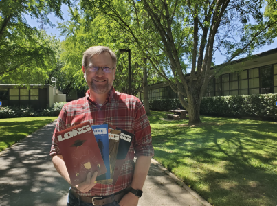 Sac State professor Daniel Bethel stands between Caleveras and Alpine Hall holding the first four volumes of his comic Long John on Tuesday, May 3, 2022. Bethel said he’s proud of these books because they reflect the two things he loves doing: English and art. 
