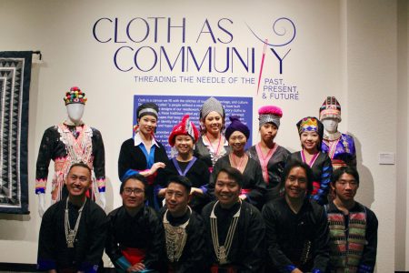 A group of models posed together in front of the “Cloth as Community” sign in the Library Gallery on Thursday, Feb. 2, 2023. The varied ensembles express Hmong culture through textiles. 