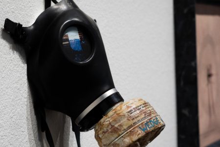 A gas mask on the wall near the entrance of the Smog Collectors exhibit at the Library Gallery Thursday, Feb. 23, 2023. The lens reveals an image depicting various agents of pollution in modern society; the inscription on the filter provides some background behind the inspiration for the piece.