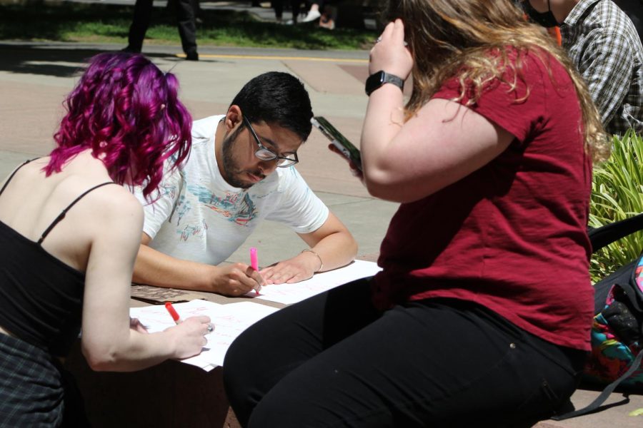 Psychology major Evin Mueller and other participants create signs in the Library Quad in protest to religious demonstrator Daniel John Lee Wednesday, May 10, 2023. Many signs were against Lee’s beliefs and Sac State student Shaun Harris said they wanted to “spread positivity on campus.”