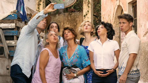 The Portokalos family arrives at Toula’s father’s village in Greece. John Corbett as Ian Miller takes out his phone for a group selfie with the family. The film is humorous and romantic and consists of family and cultural acceptance.