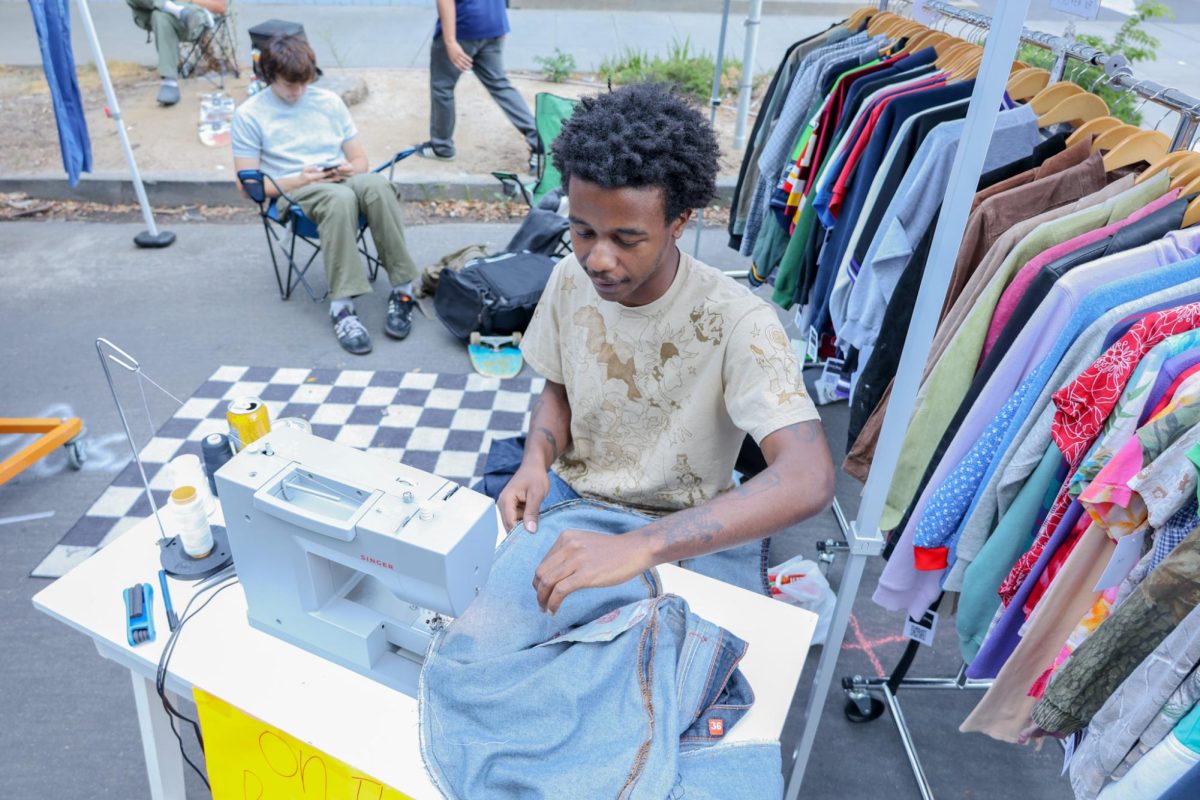 : Small business owner Emmanuel Dixon repairs a pair of jeans at the Stinger Expo on Wednesday on Saturday, Sept. 16, 2023. Dixon’s business is called ifyoucarepleasedo and sells vintage,Y2K, and modern used clothing.