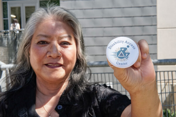 Mary Lee Vance, Director of the Disability Access Center, holds a pin featuring the center’s name and logo in front of the Academic Information Resource Center  Thursday, Sept. 7, 2023. The new Disability Cultural Center is located in room 2011 in the AIRC.