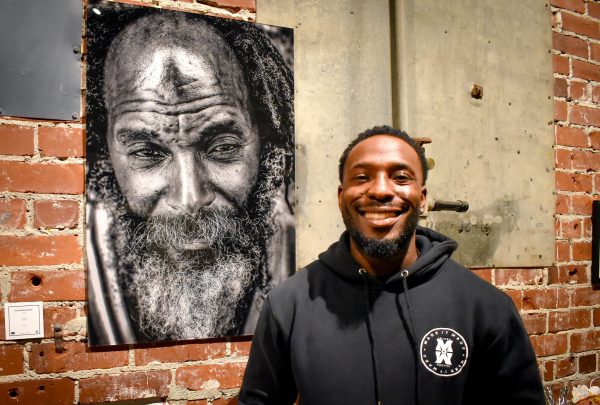 Kachiside Madu at his “Homeless to Heartfull” exhibit on Friday, Nov. 17, 2023 posed in front of his “Black Jesus” black and white portrait at the Brickhouse Gallery. His exhibit features over 8 different black and white pieces, with metal framed portraits, canvas and prints.