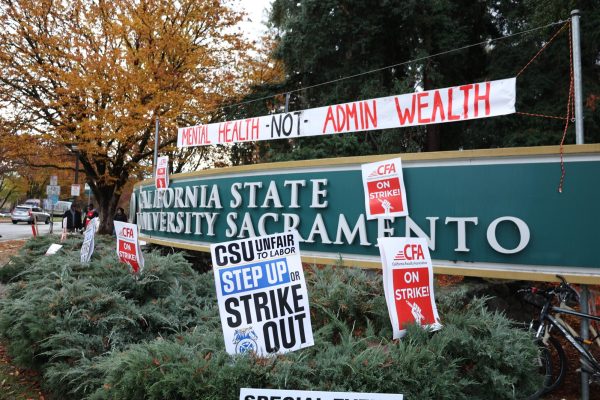 Protestors cover the Sacramento State sign in red and white CFA posters during the initial CFA strike Thursday, Dec. 7, 2023. Strikers held signs demanding better pay and better mental health accommodations for students and staff alike.