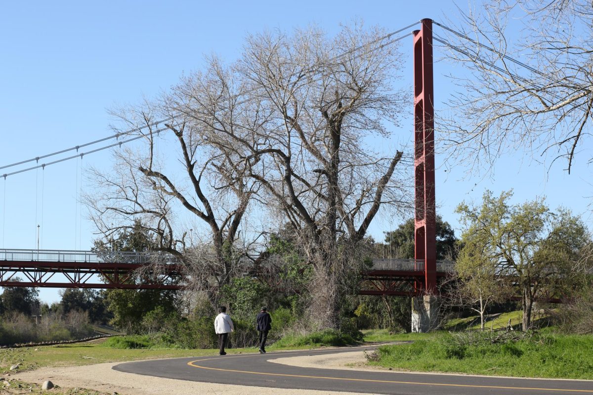 Two people take a stroll along the Jedediah Smith Memorial Trail with a view of Sac State’s Guy West Bridge in the foreground Thursday, March 14, 2024. Many students often walk or bike the different trails near campus.