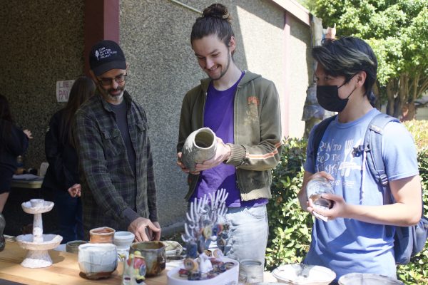 Ceramics Guild faculty advisor Scott Parady and junior art major Cyrus Hunter are among students observing ceramic pieces on display at the Ceramics Guild ceramic sale Tuesday, April 30, 2024.  Community members of varying experience levels are encouraged to join.