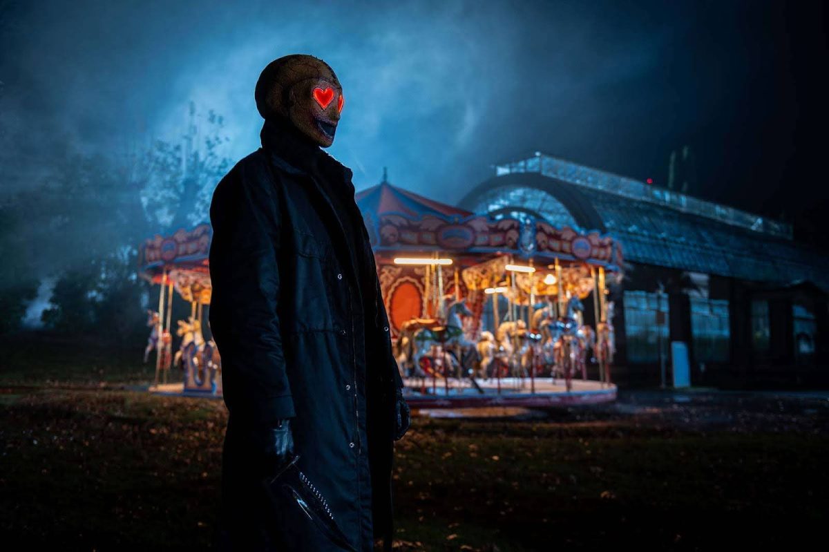 The red heart-shaped eyes of the killer glow as he stands near a carnival carousel in Josh Ruben’s “Heart Eyes” (2025). The film blends classic, early 2000s horror tropes with a modern-day lens and Valentine's Day coat of paint. (Photo courtesy of Sony)