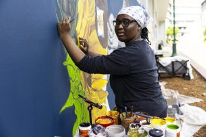 Bachelor of Fine Arts in Studio Art alumna Amari Moore works on her mural, carefully painting fine details on her sunflower on the south wall of the Ernest E. Tschannen Engineering Teaching and Research Building, Tuesday, Sept. 9, 2025. She will exhibit her other works at the Sojourner Truth African Heritage Museum in October. 