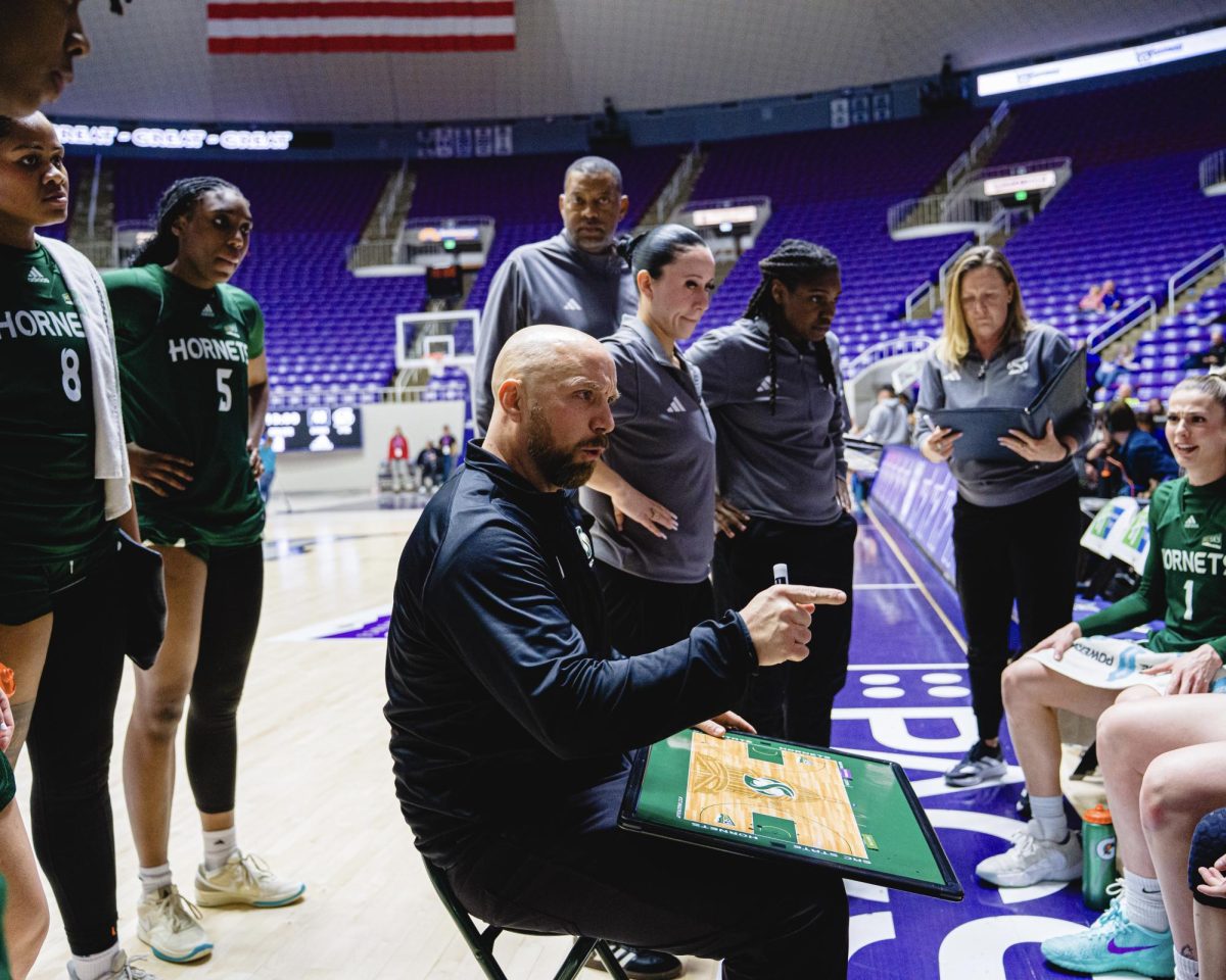 Head coach Aaron Kallhoff sits in the middle of a circle of his players, discussing plays against Weber State Monday, Feb. 3, 2026. The Hornets ultimately failed to close out after cutting a 16-point lead, losing 72-64.