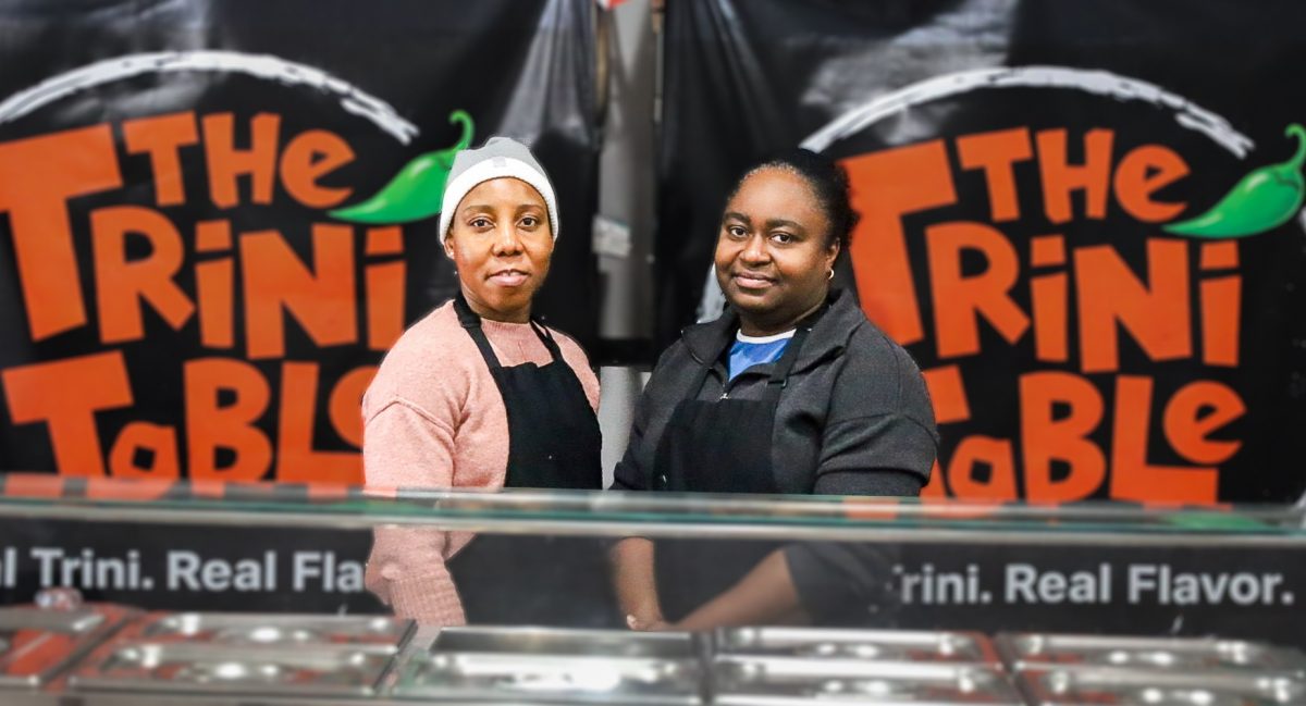 Tammi Ifill (left) and Eda Kendall (right), co-owners of The Trini Table, pose for a picture in their restaurant Wednesday, Feb. 18, 2026. Above their heads is the flag of the twin islands of The Republic of Trinidad and Tobago, where the couple were born and raised. 