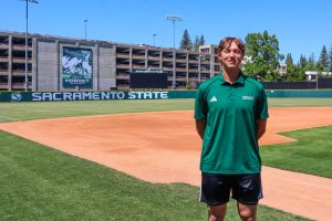 Senior pitcher Ethan Lay stands in front of the scoreboard at John Smith Field ahead of practice Thursday, April 30, 2026. Lay has dominated in his time with the green and gold, rising to be the team’s Friday night starter.