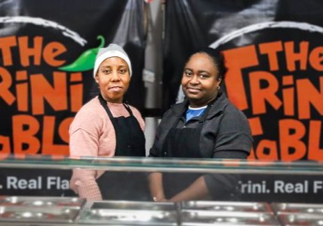 Tammi Ifill (left) and Eda Kendall (right), co-owners of The Trini Table, pose for a picture in their restaurant Wednesday, Feb. 18, 2026. Above their heads is the flag of the twin islands of The Republic of Trinidad and Tobago, where the couple were born and raised. 